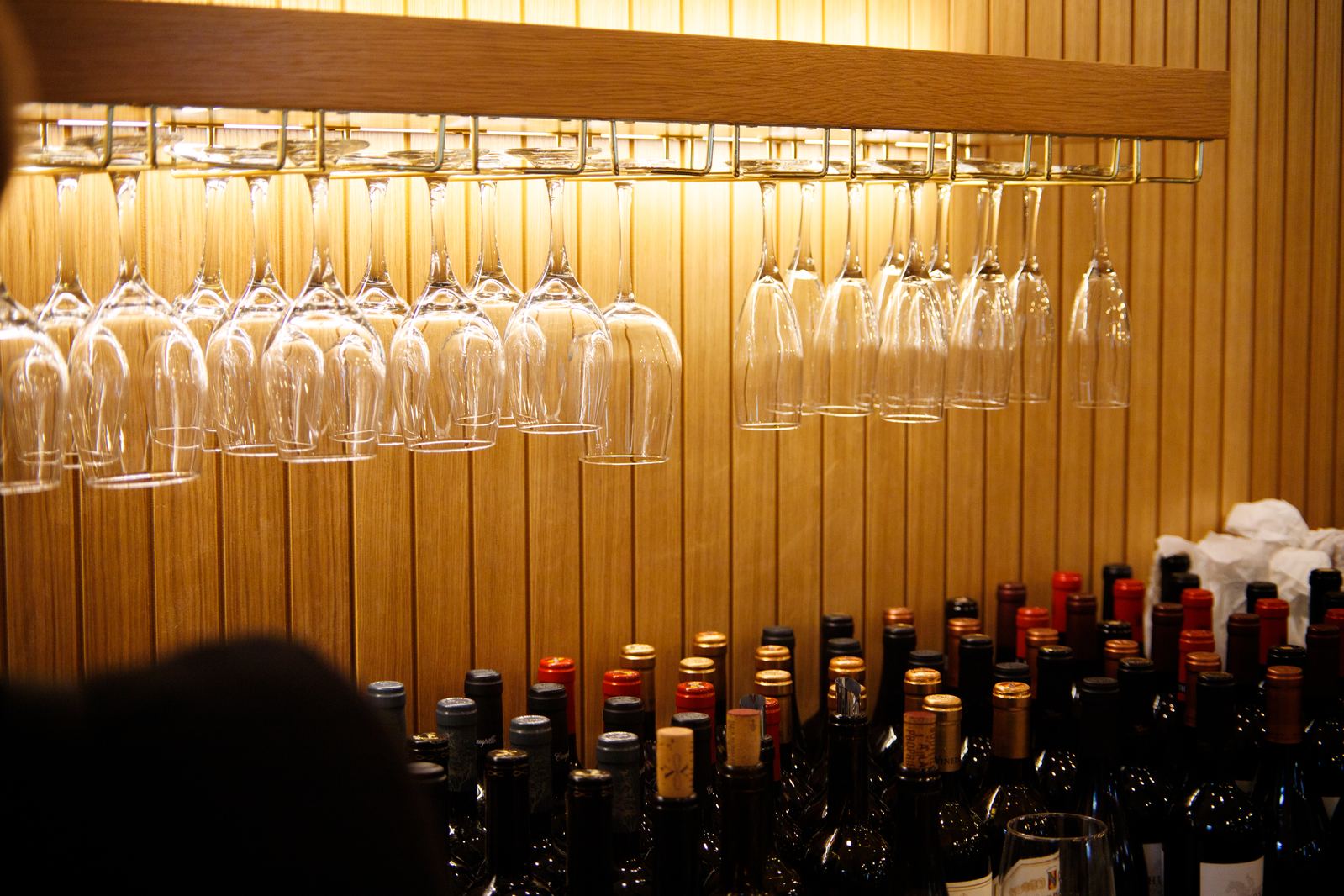 Wine bottles and hanging glassware along the wood-paneled wall at Solera Kitchen + Wine Bar in Seal Beach